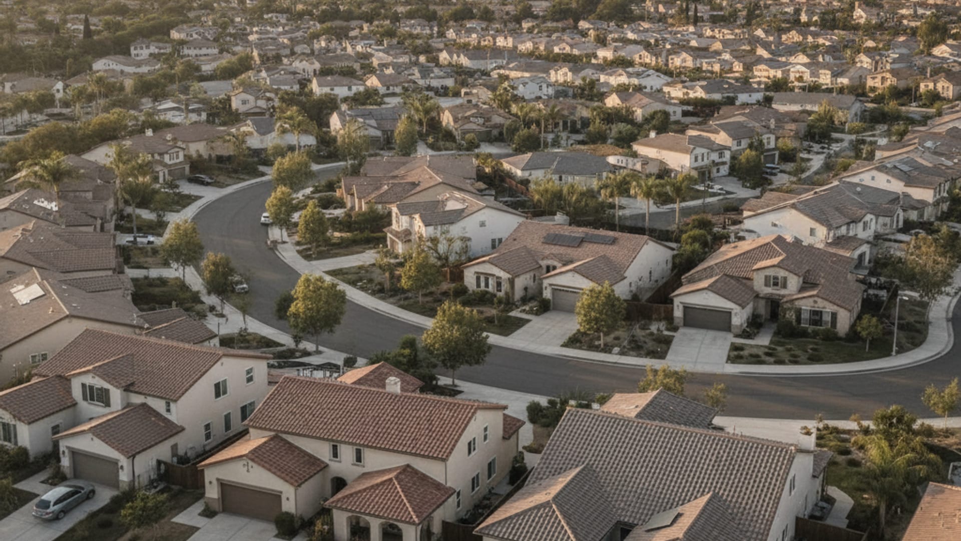 Aerial view of a San Diego County residential neighborhood showing tile and shingle roofs with mountains in the background at golden hour